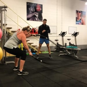 woman doing battle ropes while personal trainer times her