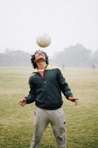 cross training man in misty field bouncing soccer ball above head