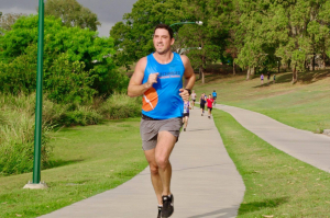 man in blue singlet running along green park
