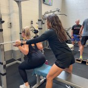 personal trainer assisting another woman with a weights bar