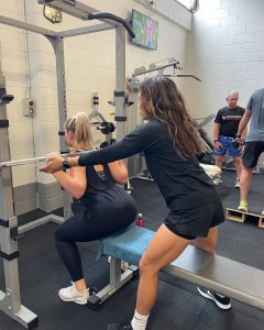 personal trainer assisting another woman with a weights bar