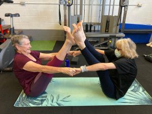 two older women stretching their legs together in a V shape