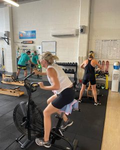 woman on exercise bike with man working out near mirror in background