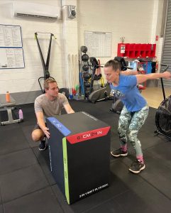 woman about to jump on a box with personal trainer watching