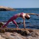 woman doing a backwards yoga pose on a rock by the ocean
