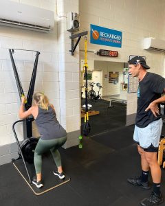 woman using skierg machine while a personal trainer supervises