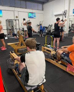 two men on a rower, other people using weights