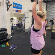 woman in singlet lifting weight over her head in gym studio