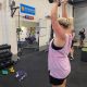 woman in singlet lifting weight over her head in gym studio