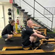 personal trainer encouraging two people using rowing machines side by side