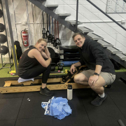 personal trainer crouched next to a woman on a rowing machine. Both are smiling.