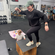 woman stepping up onto box in studio gym while toddler stands next to her.
