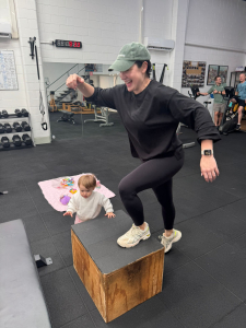 woman stepping up onto box in studio gym while toddler stands next to her.
