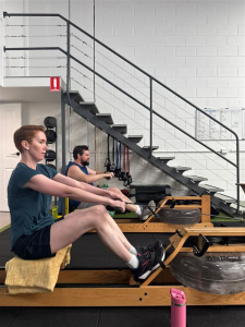 a man and a woman on the rowing machines in a small studio