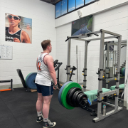 man in upright position holding bar of weights, looking in mirror