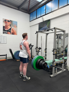 man in upright position holding bar of weights, looking in mirror
